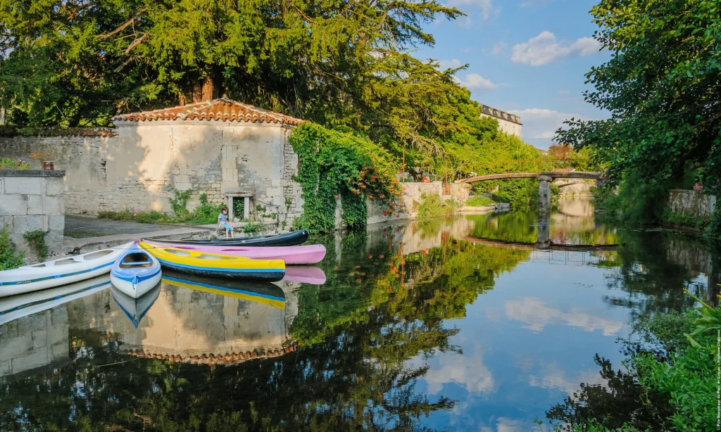 Canoes on the banks of the Charente at Bassac, with a small bridge and Saint Pierre abbey in the background