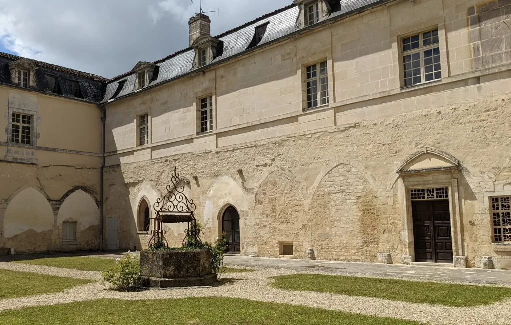 Cloitre de l'abbaye Saint Etienne dans le village de Bassac, au centre un puits avec un décor en fer forgé entouré de rosiers