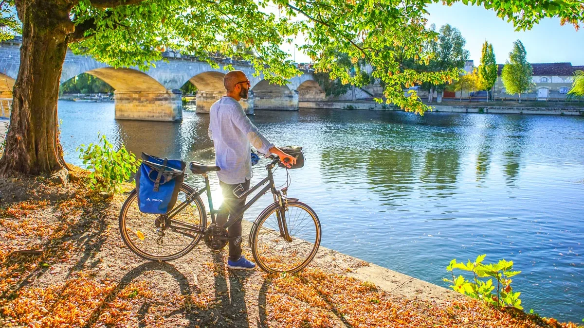 La Flow Vélo itinéraire dédié aux mobilités douces le long de la Charente à Cognac, cycliste admirant la vue sur le Pont Saint Jacques et les quais de Cognac