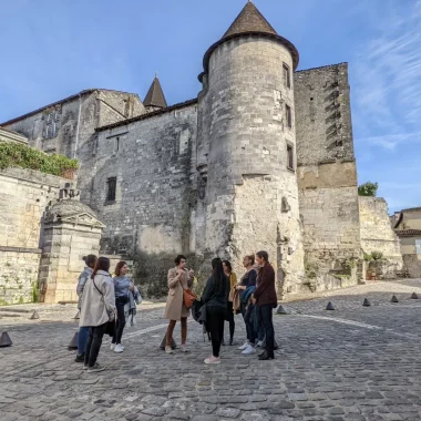 Visite guidée Cognac du Moyen age à nous jours avec un groupe de personnes par Nath, guide de l'Office de Tourisme de la Destination Cognac dans les rues pavées de la vieille ville de Cognac à l'arrière du chateau royal de Cognac et de la Fontaine François 1er