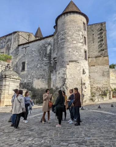 Visite guidée Cognac du Moyen age à nous jours avec un groupe de personnes par Nath, guide de l'Office de Tourisme de la Destination Cognac dans les rues pavées de la vieille ville de Cognac à l'arrière du chateau royal de Cognac et de la Fontaine François 1er