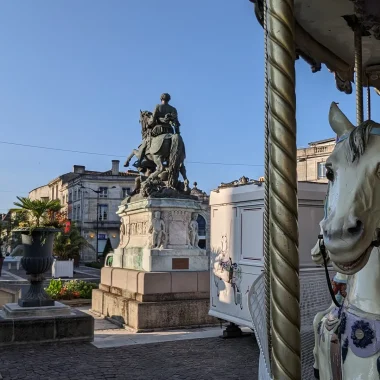 La place François 1er à Cognac où trône la statue équestre de François 1er, au premier plan les terrasses des cafés et le carrousel avec ses chevaux de bois