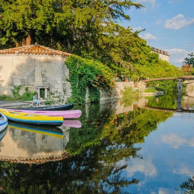 Canoës en bord de Charente à Bassac en arrière plan un petit pont et l'abbaye Saint Pierre