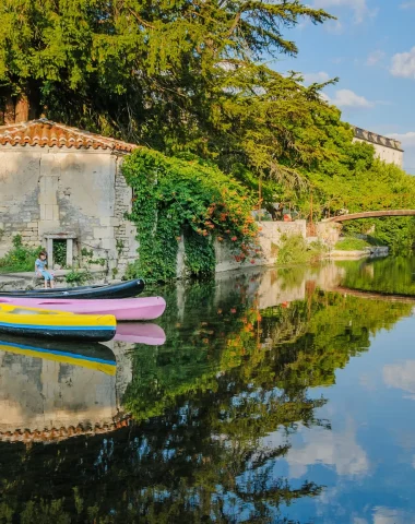Canoes on the banks of the Charente at Bassac, with a small bridge and Saint Pierre abbey in the background